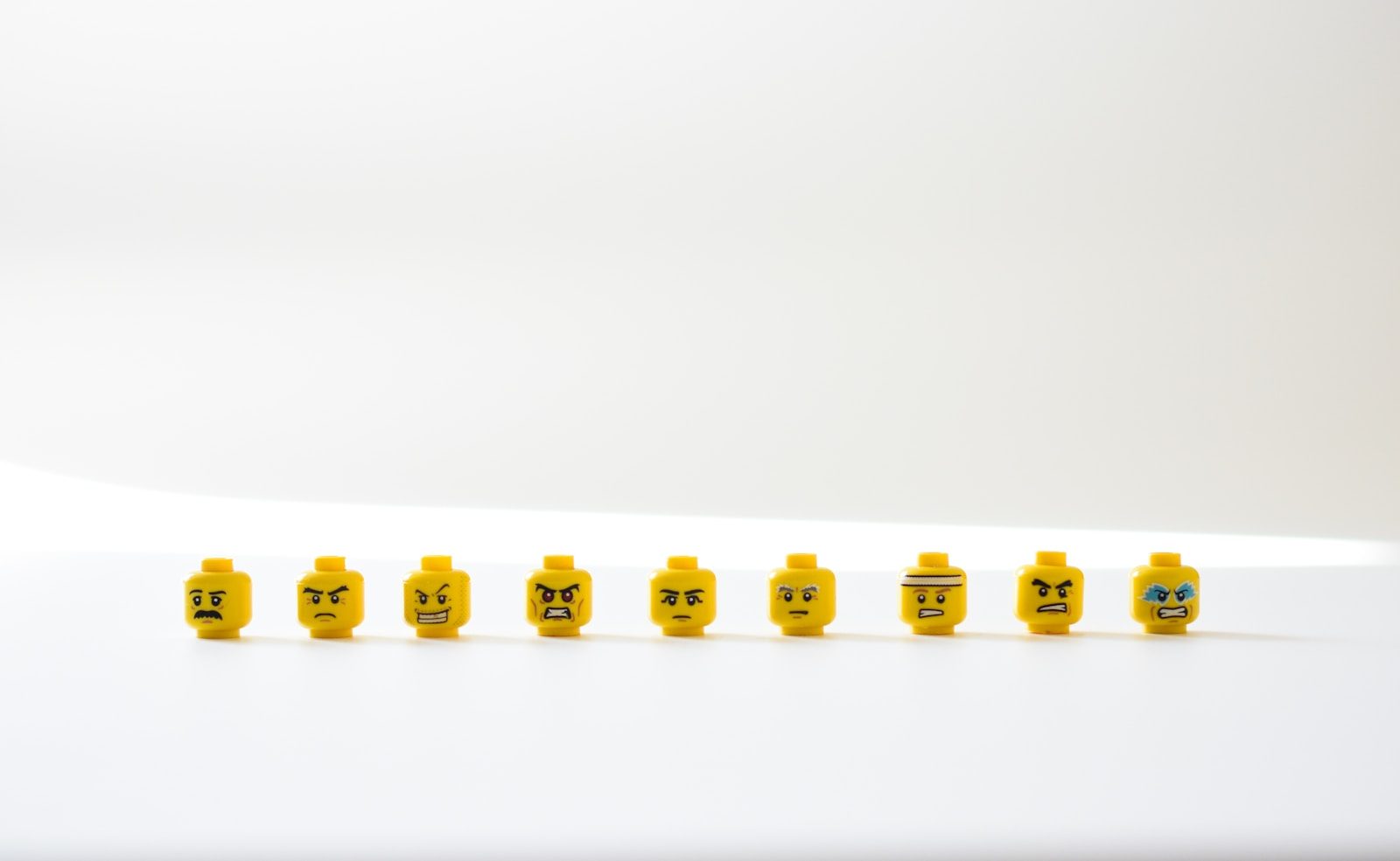 Nine yellow toy heads with different facial expressions in a row on white